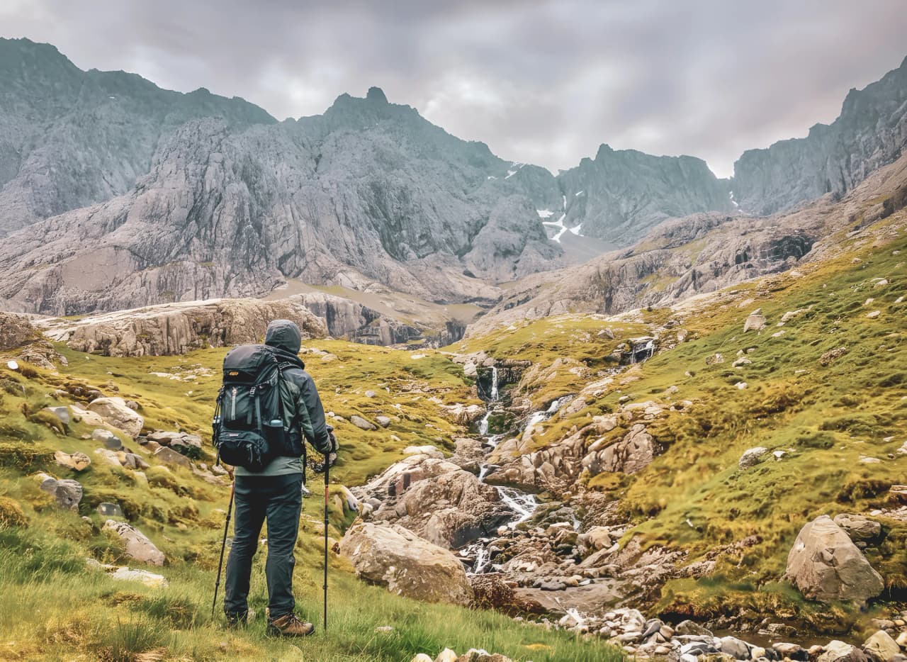 A walker contemplating majestic mountains and green valleys in Scotland.