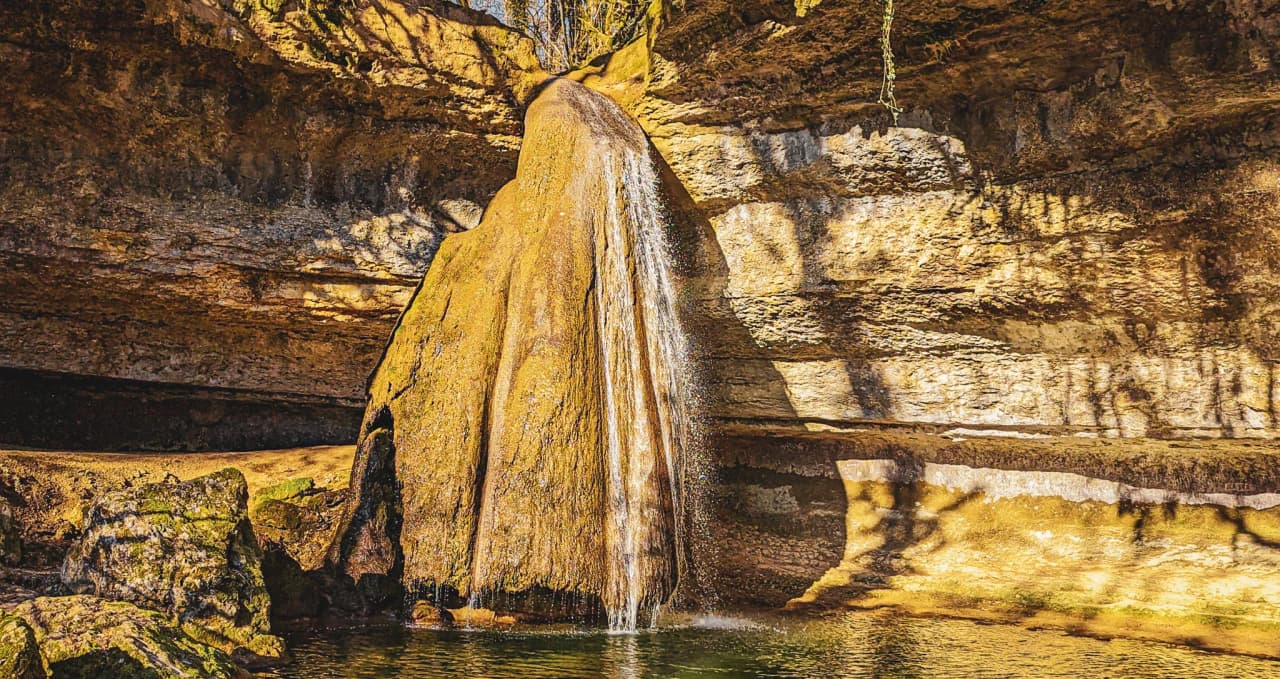 Spectacular waterfall flowing into a shaded pool, surrounded by golden stones.