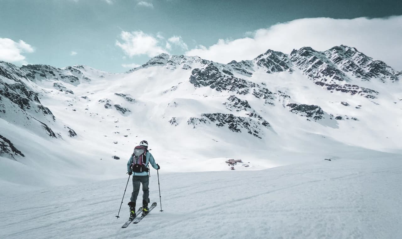 Skieur de randonnée sur un vaste glacier, avec des montagnes enneigées en toile de fond.