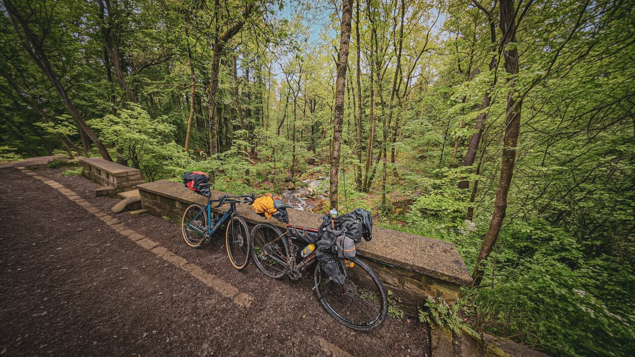 Twee fietsen op een houten bankje, omgeven door weelderig groen en naast een vredig beekje.