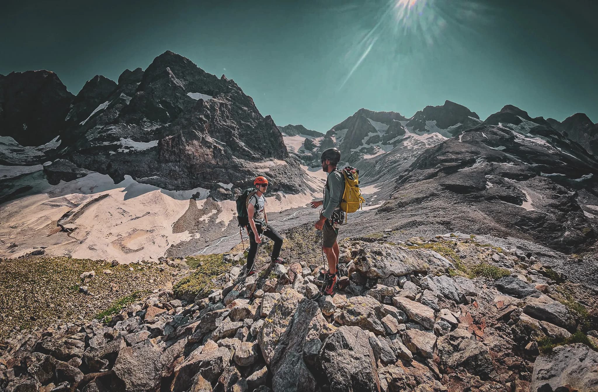 Deux alpinistes discutent sur un sentier rocheux, avec des sommets majestueux en arrière-plan.