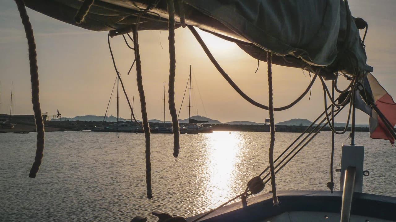 Vue apaisante depuis un bateau, reflet doré sur l'eau, voiles blanches et criques sauvages en toile de fond.