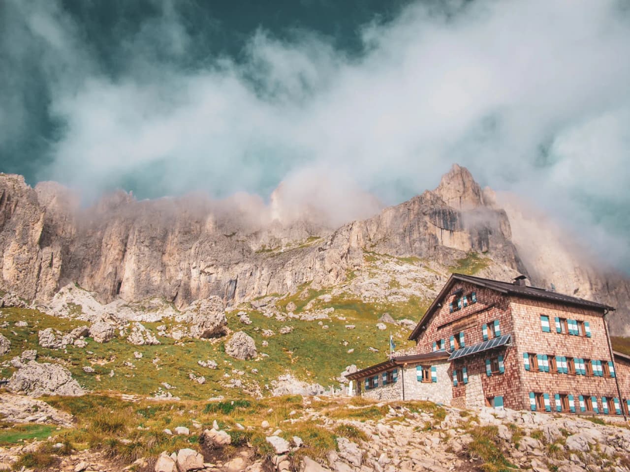 A rustic Mountain hut at the foot of the Dolomites, surrounded by majestic panoramas and light clouds.