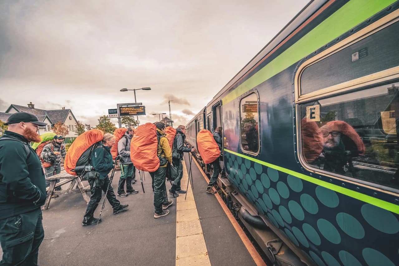 Een groep wandelaars op weg naar de Highlands, klaar voor een avontuur met de trein, kleurrijke tassen op hun rug.