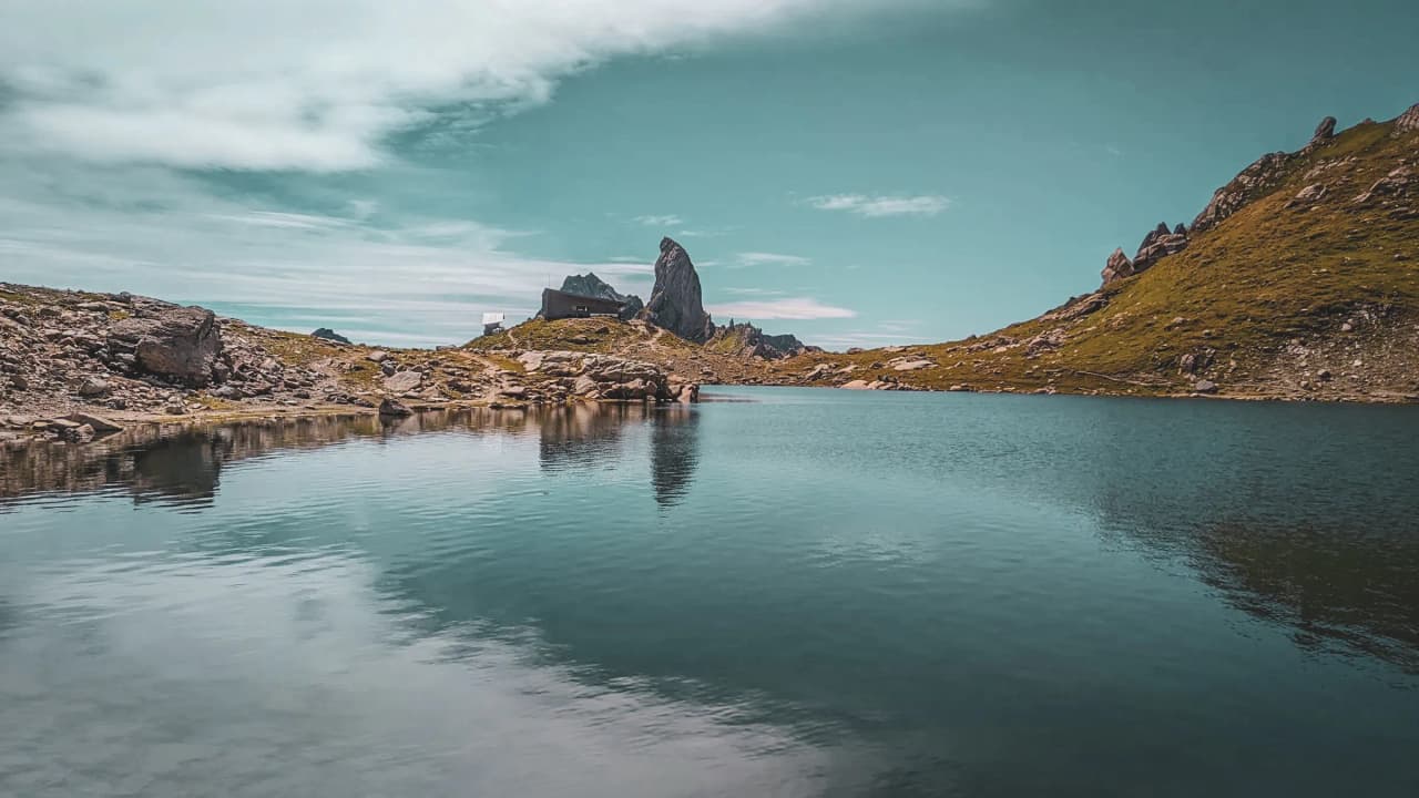 Lac alpin entouré de rochers et d'herbe verdoyante, avec un ciel bleu éclatant.