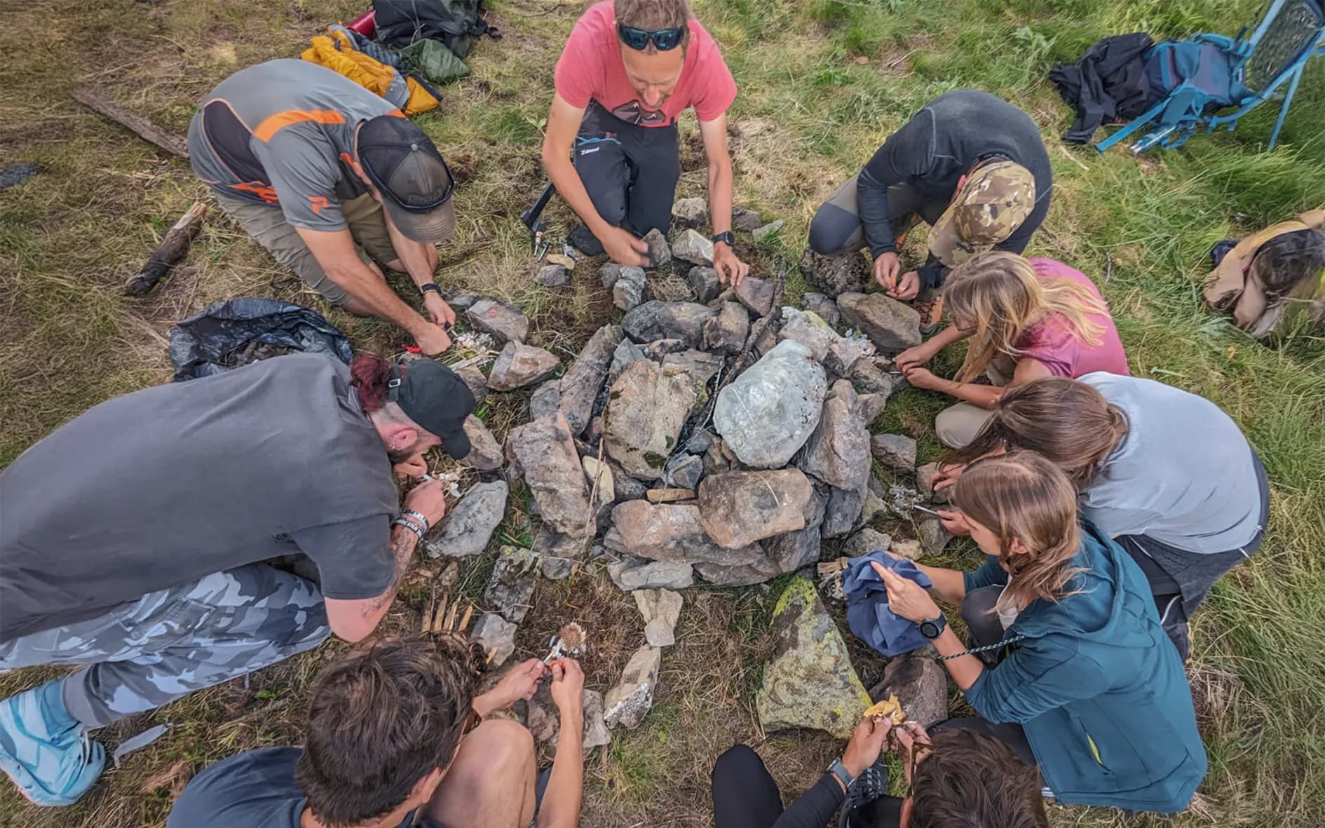Group of people around a wood fire with lots of stones in the middle.