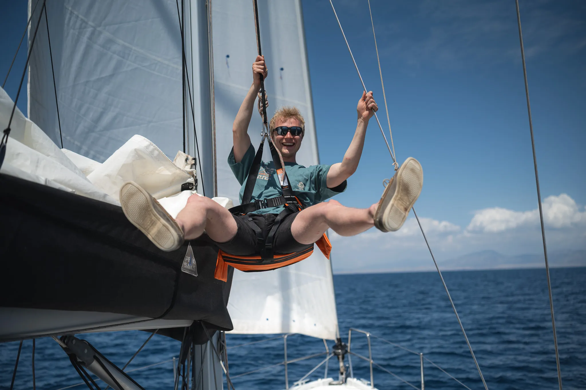 Un jeune homme souriant en train de naviguer à la voile, profitant des eaux cristallines grecques.