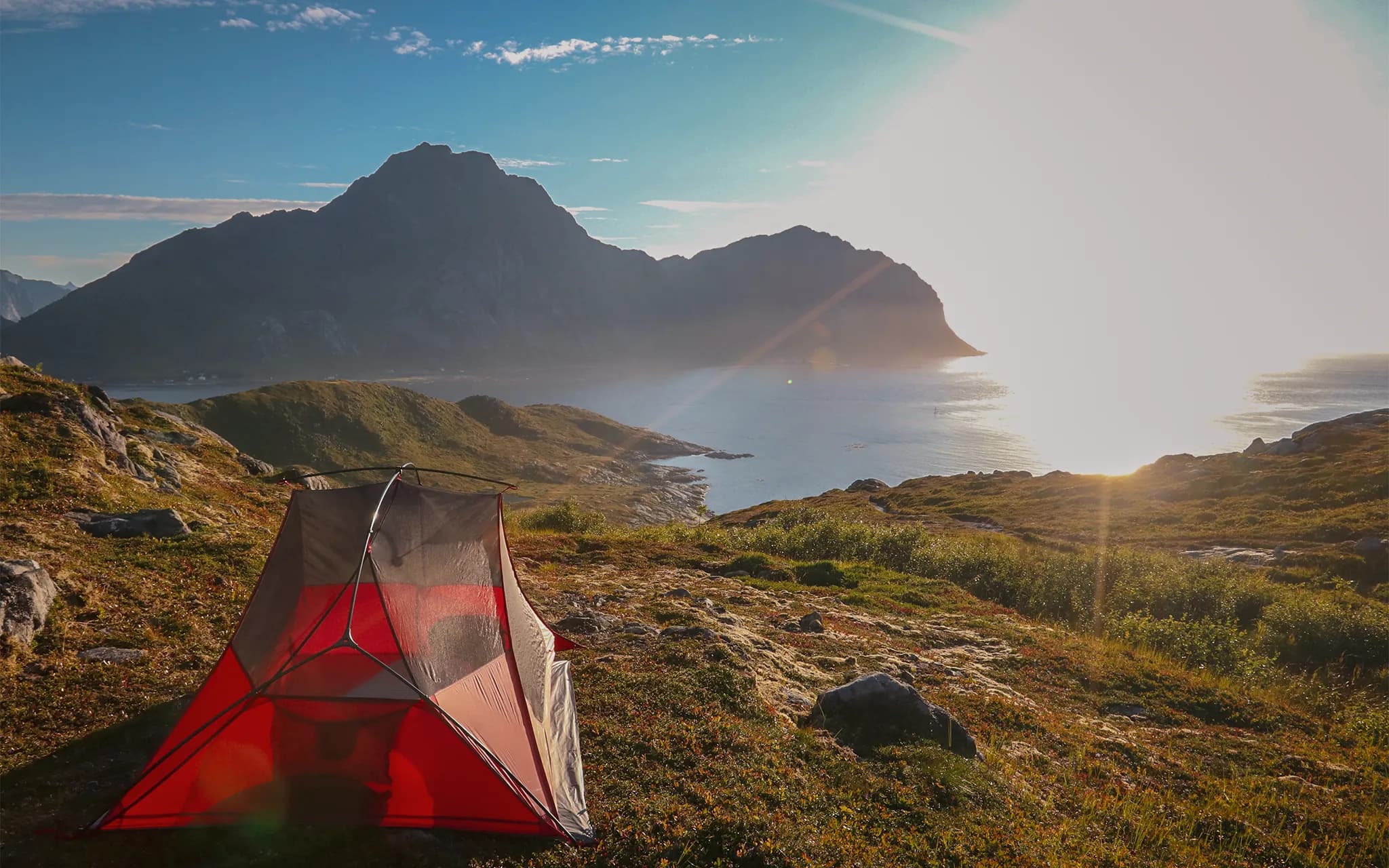 Bright red tent overlooking the sparkling sea, with majestic mountains in the background.