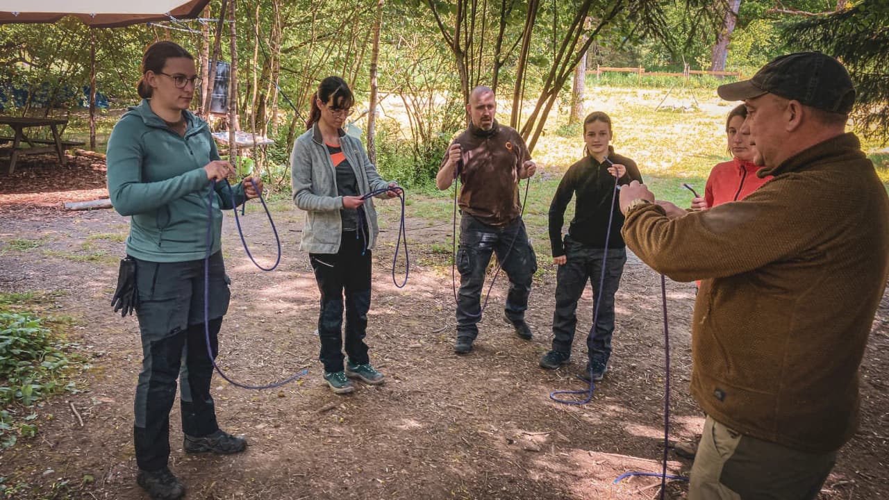 Participants d'un stage de survie en forêt, apprenant à nouer des cordes dans la nature verdoyante.