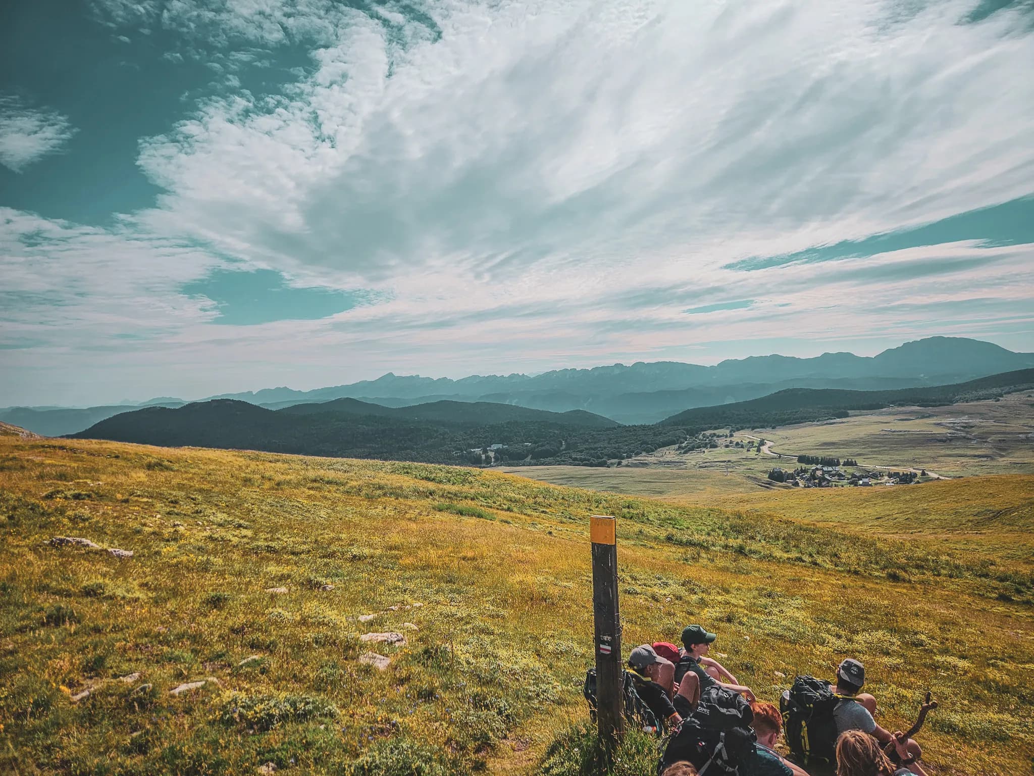 A captivating mountain landscape with lush green valleys stretching as far as the eye can see. The ground is covered with yellow grass and rocky features, while in the distance, mountains loom large.