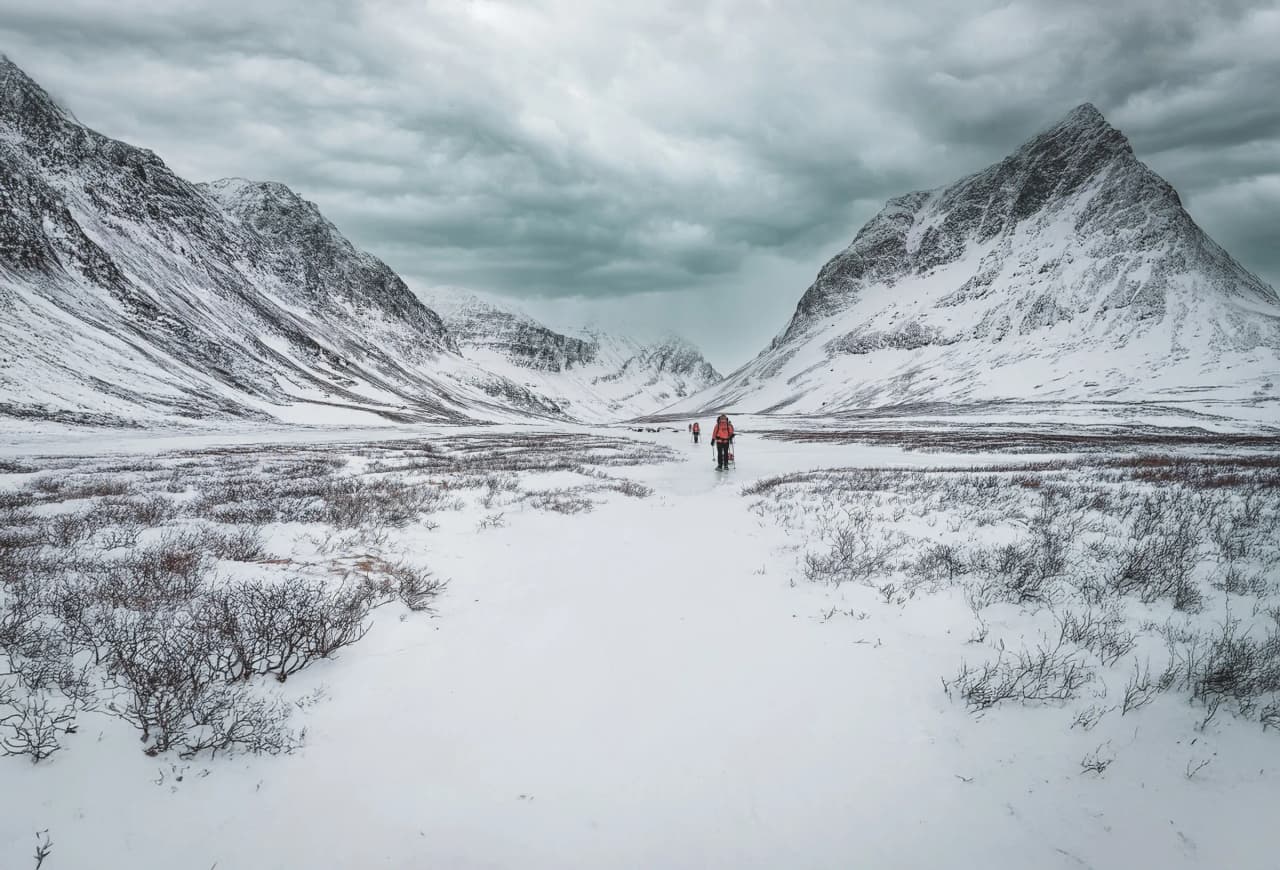 Hikers on snowshoes make their way through a snow-covered landscape, surrounded by majestic mountains.