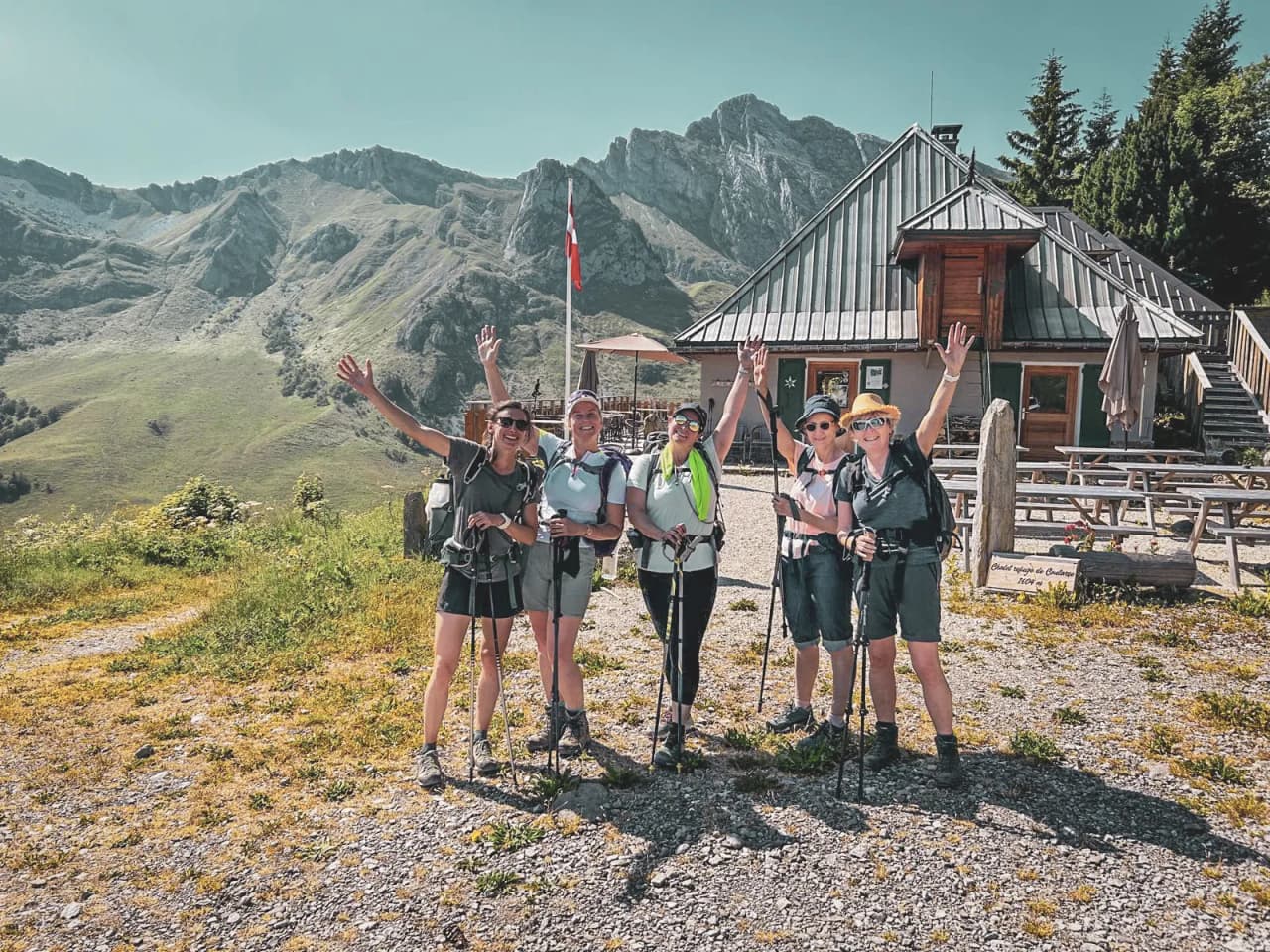 A group of smiling hikers in front of an alpine Mountain hut, with majestic peaks in the background.
