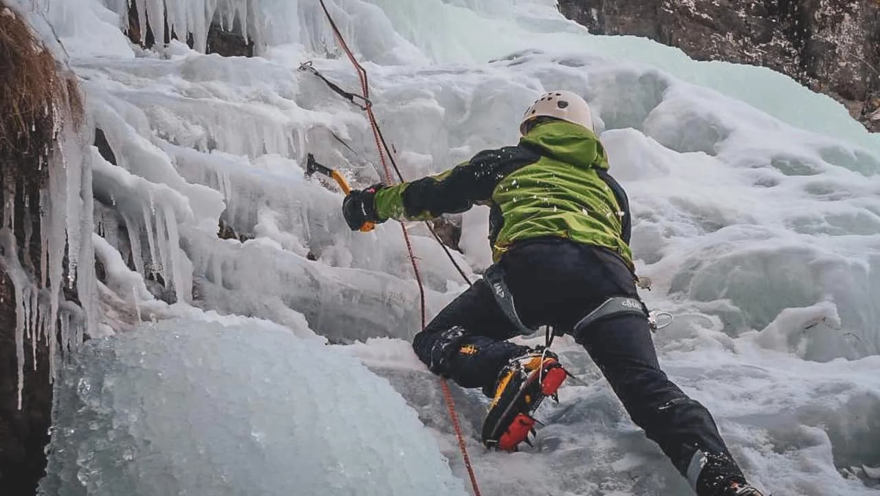 Un alpiniste grimpe une cascade de glace, entouré de paysages alpins majestueux.