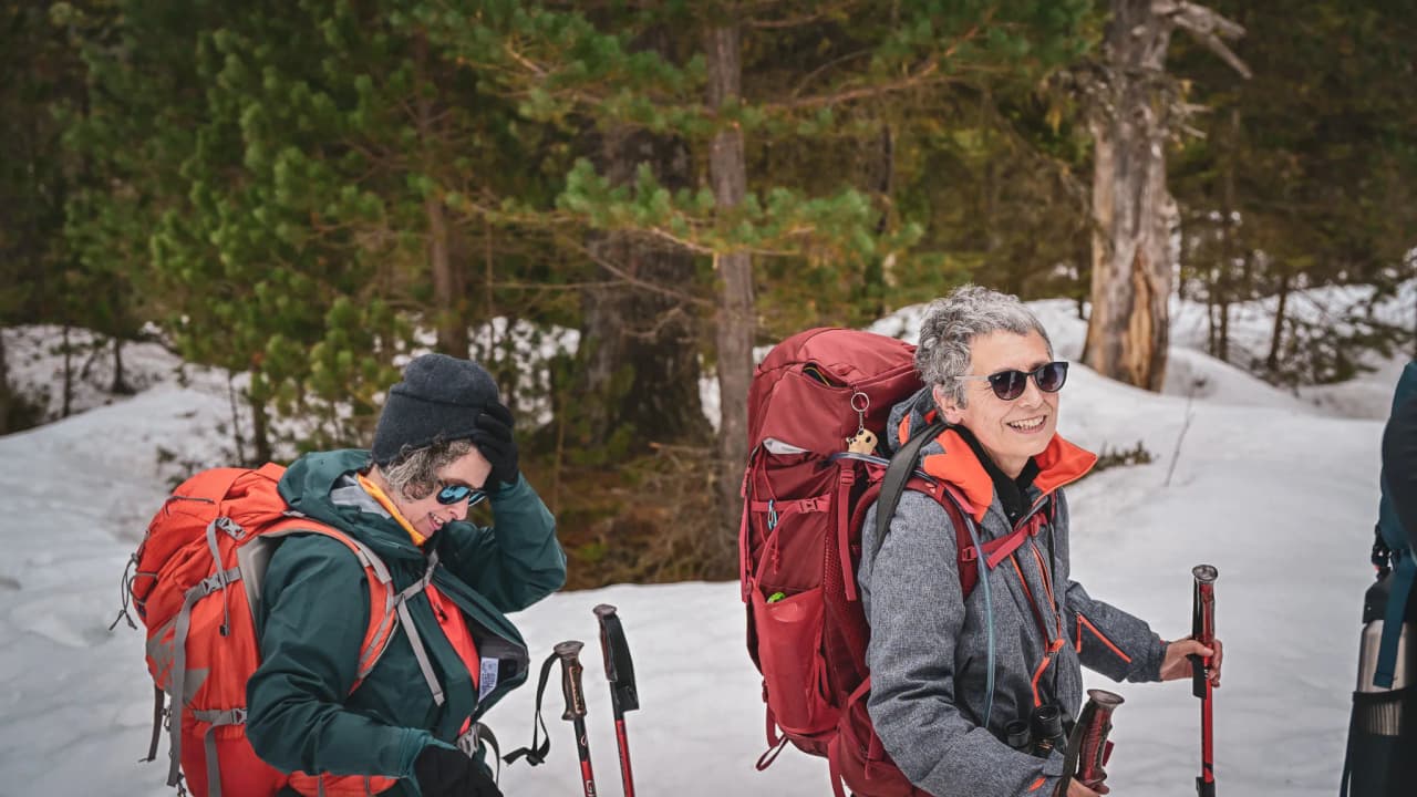 Two hikers on snowshoes smile, surrounded by the snow-covered forests of the Pyrenees.