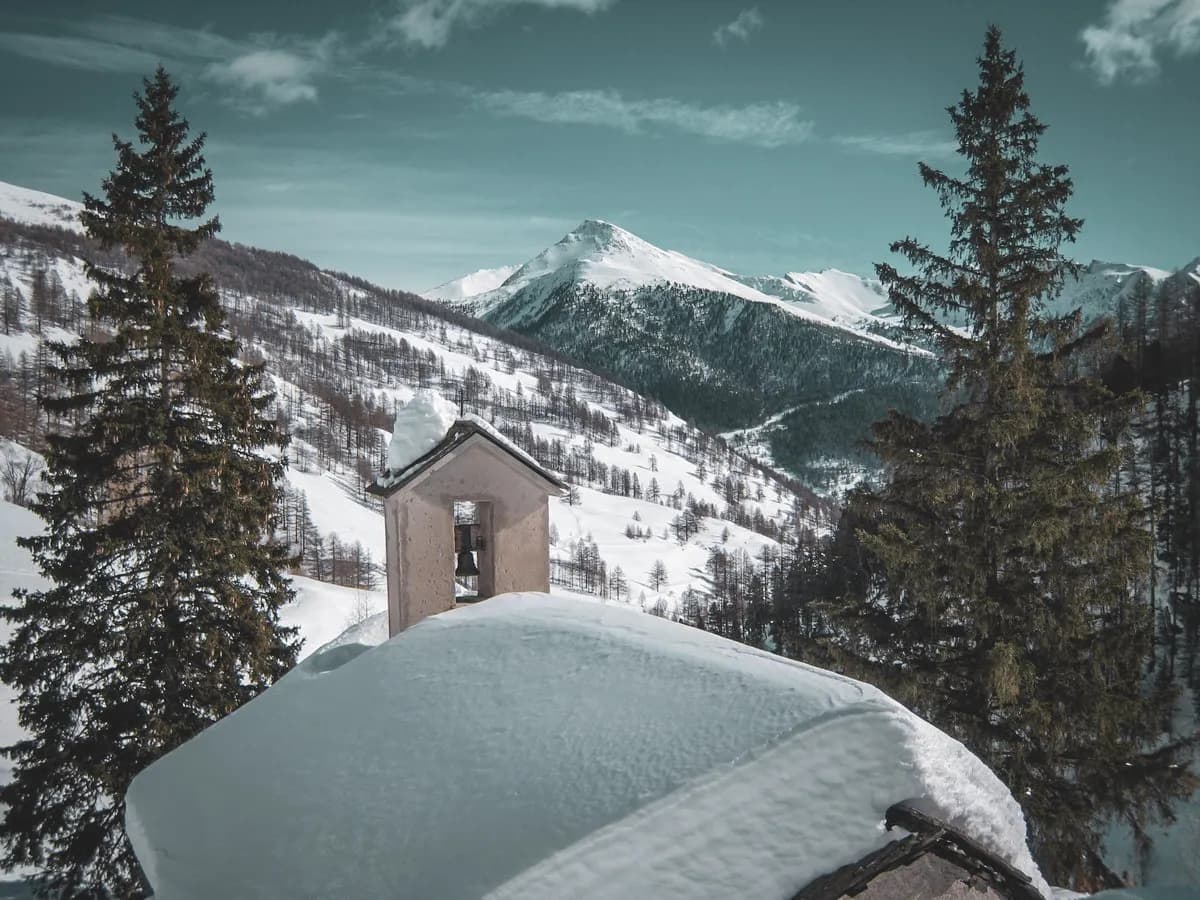 Paysage alpin enneigé avec un clocher, entouré de sapins, invitant à l'aventure en ski.