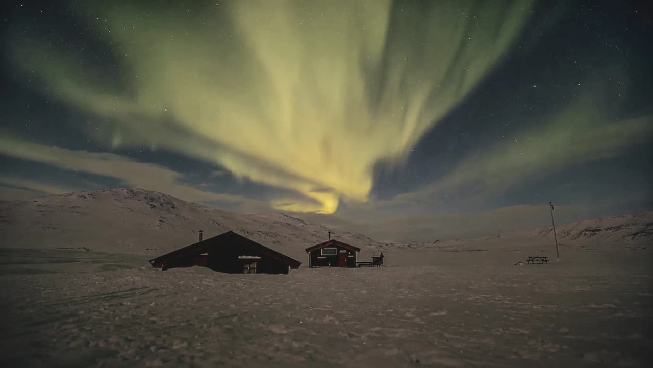 Een sterrenhemel, verlicht door het noorderlicht, boven hutten in Noors Lapland.