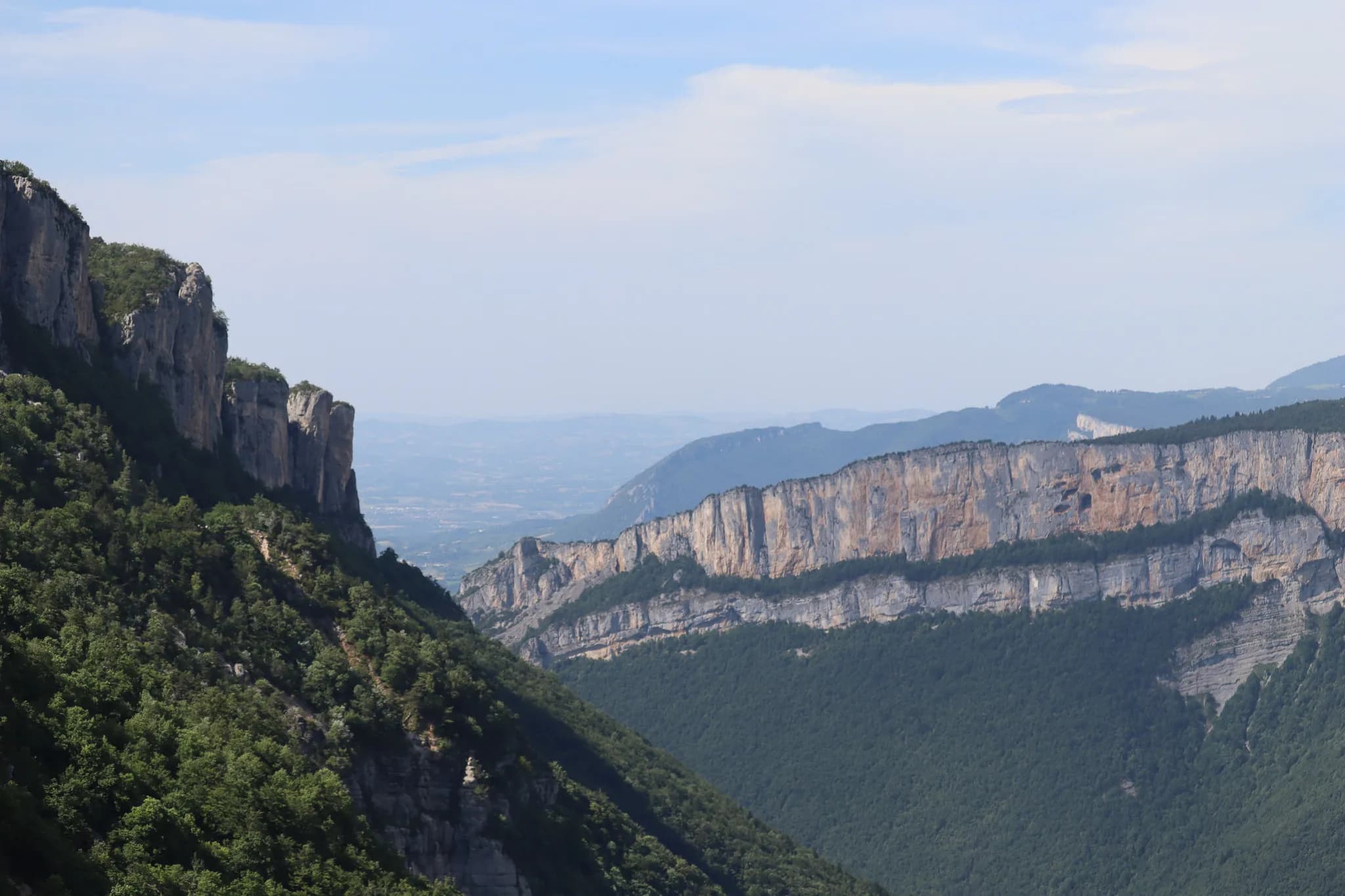 A mountainous landscape with steep, green cliffs, framed by dense forests. To the left, a rocky ridge rises steeply, while to the right, a steep, stratospheric landscape.