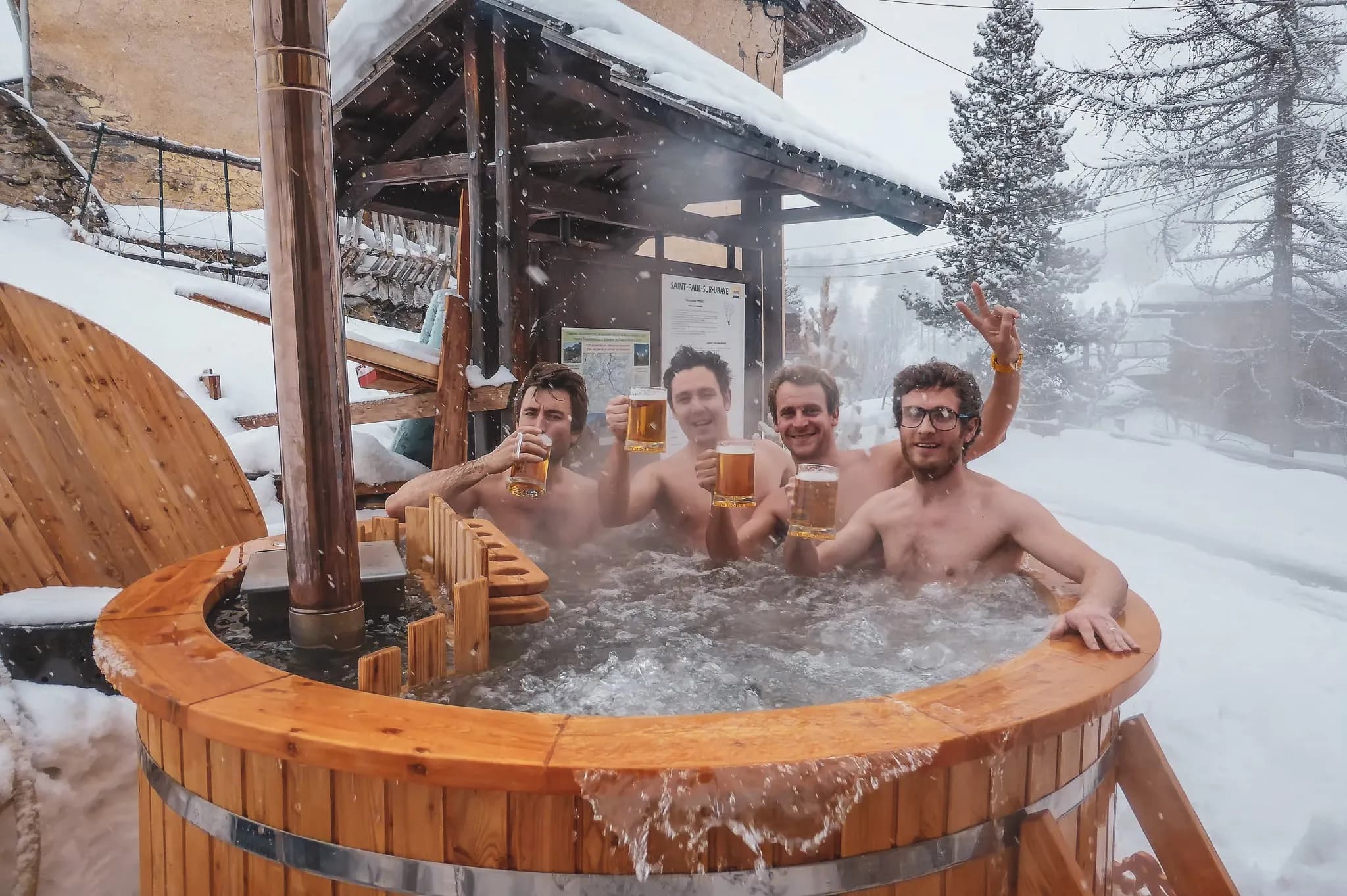 Vier vrienden ontspannen in een hot tub buiten, omringd door sneeuw en bergen.