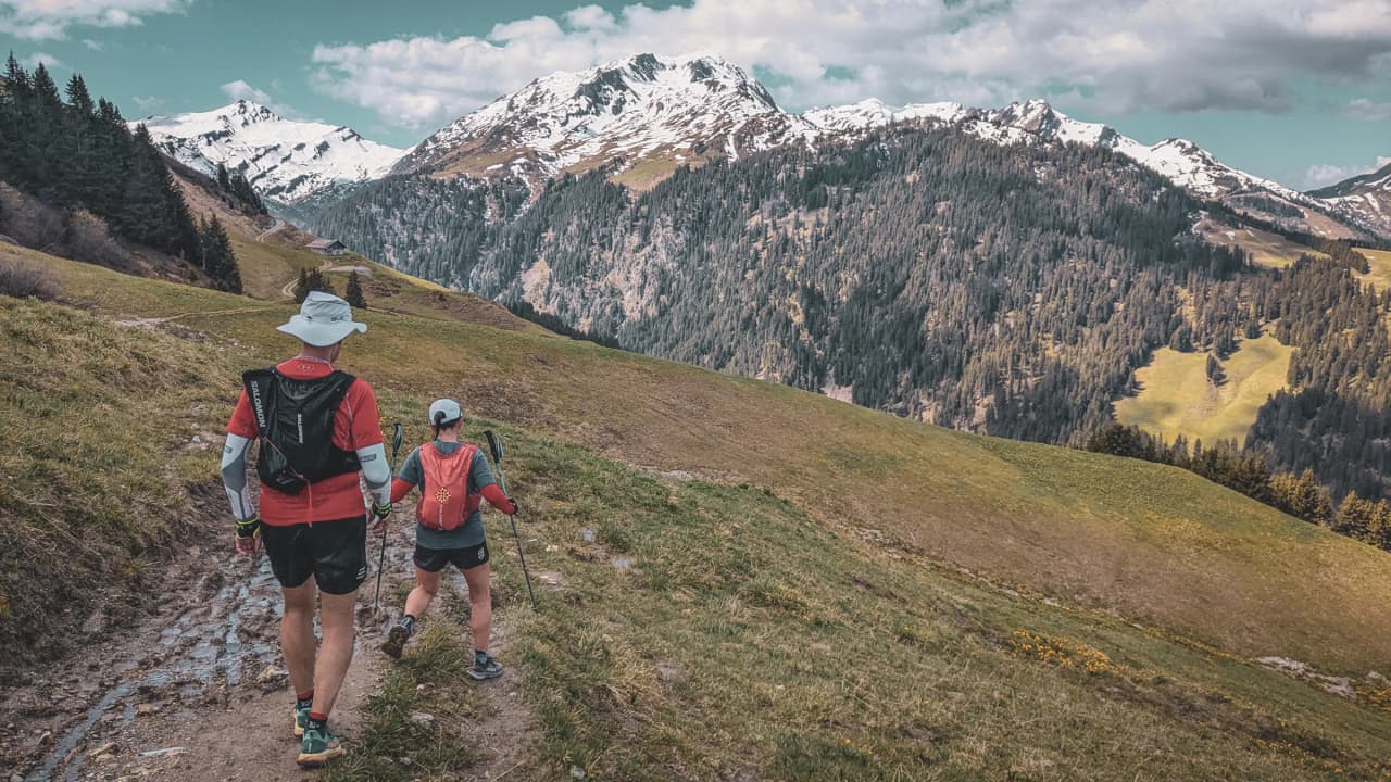 Des coureurs en trail sur un sentier verdoyant, avec les majestueux sommets enneigés en arrière-plan.