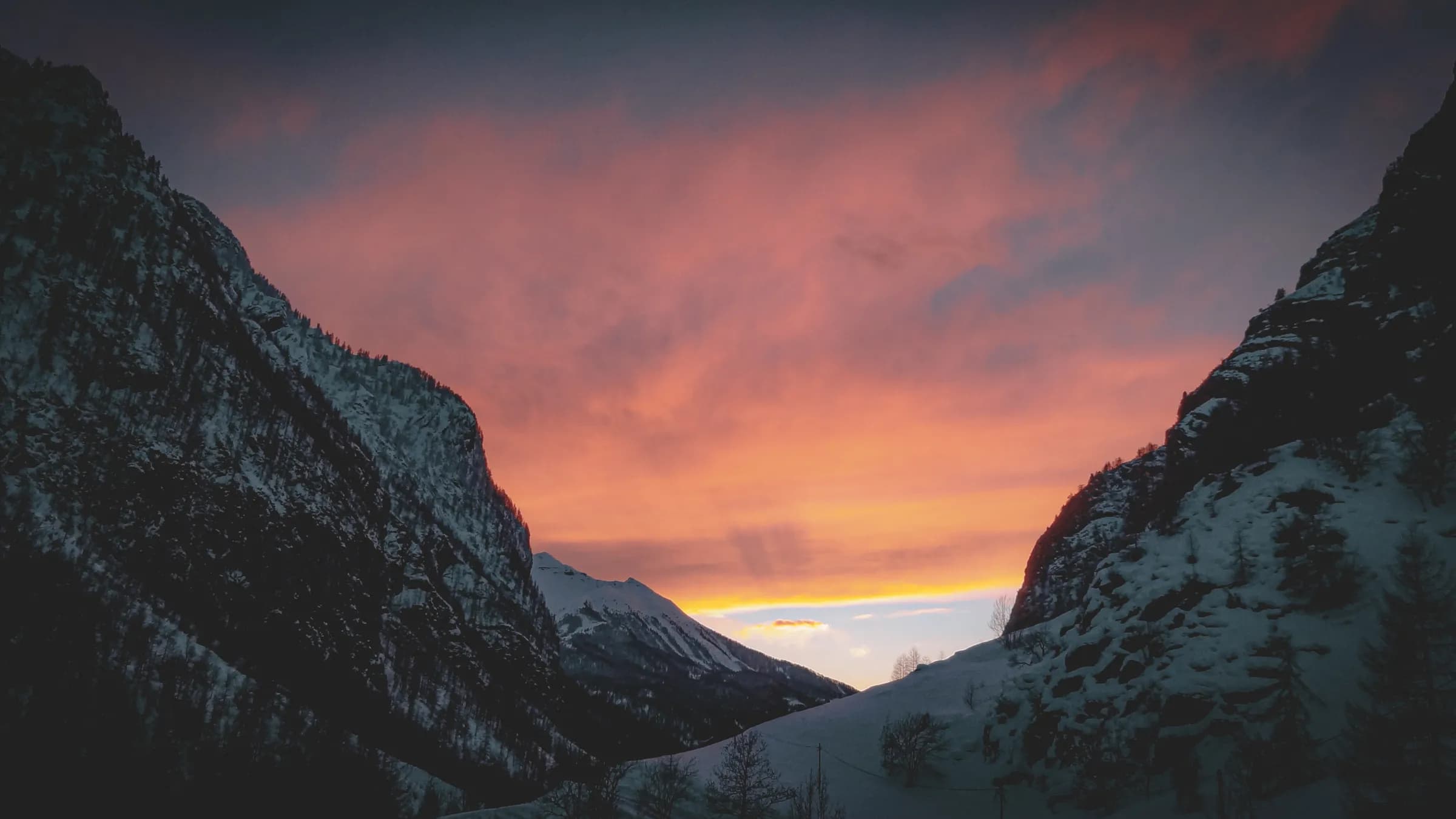 A mountainous landscape under a twilight sky, with snow-capped peaks to the left and right. The sky is coloured in shades of pink, orange and blue, creating a serene and majestic atmosphere.