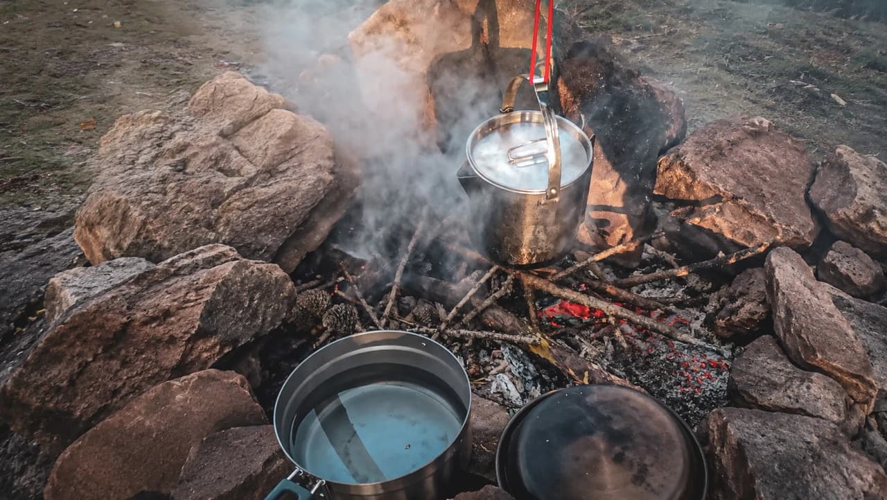 Un feu de camp avec une casserole fumante, entouré de pierres, évoquant l'aventure en pleine nature.