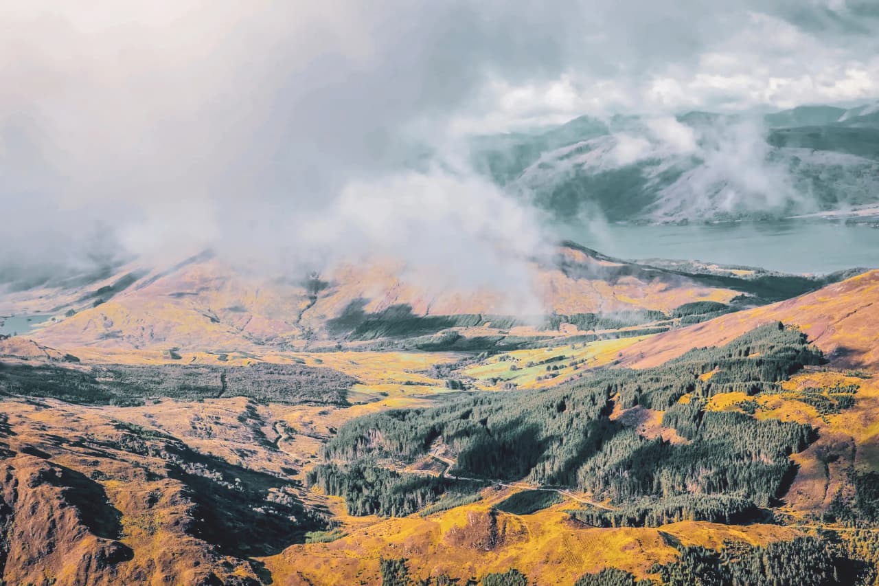 Een uitgestrekt panorama van de Schotse Hooglanden, waar bergen en valleien zich mengen in de wolken.