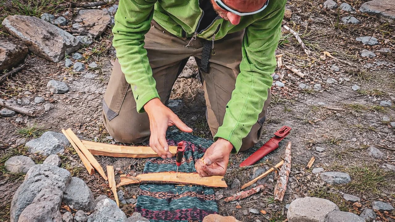 Un homme en pleine nature, créant du feu avec des outils, entouré de pierres et de forêt.