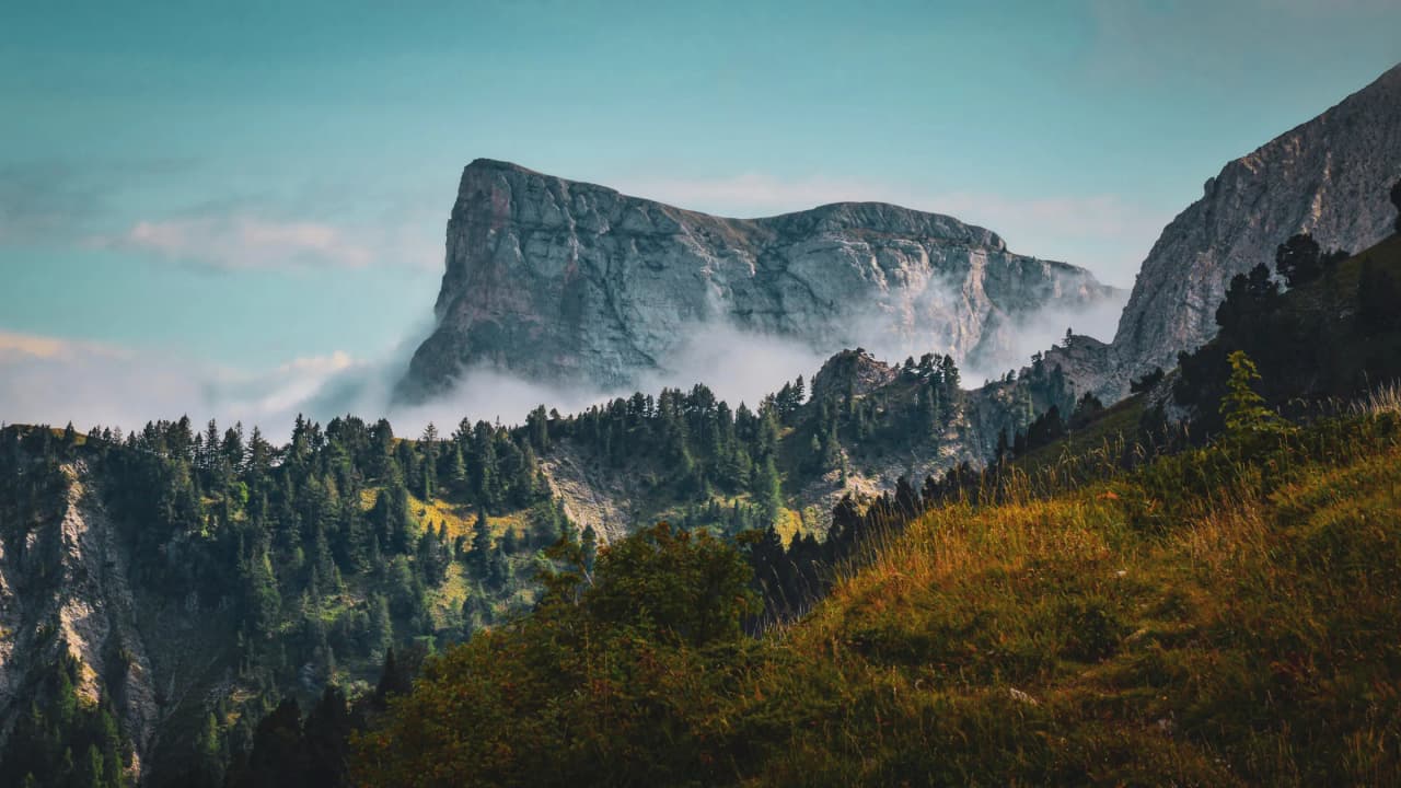 Pic majestueux émergeant des brumes, entouré de forêts verdoyantes et alpages paisibles.