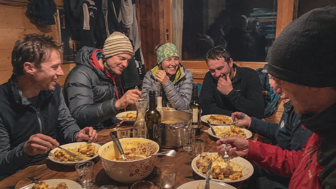 Groupe d'amis partageant un repas chaleureux en refuge après une aventure en montagne.