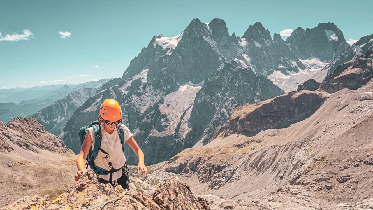 Alpiniste grimpant sur un sommet des Écrins, avec des montagnes majestueuses en arrière-plan.