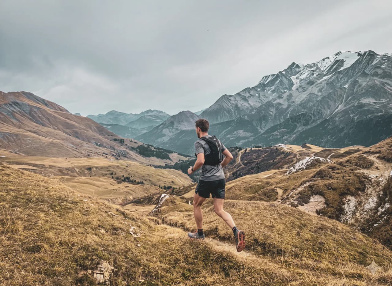 Un coureur traverse des paysages alpins majestueux, entre montagnes et vallées verdoyantes.
