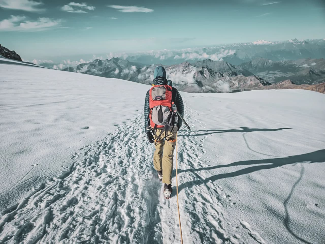 Mountaineer walking on a glacier, with majestic mountains in the background.