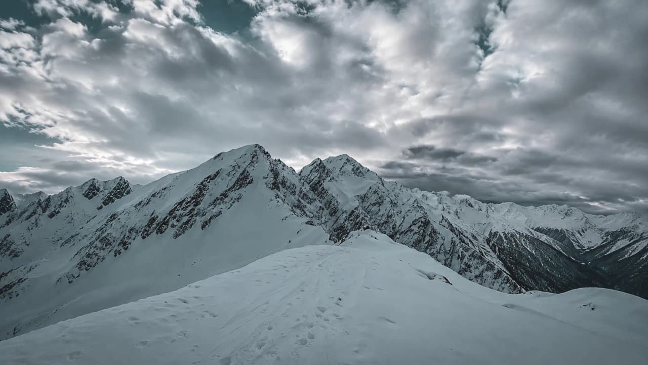 Majestic snow-capped mountains beneath a cloudy sky – an invitation to escape on a ski tour.