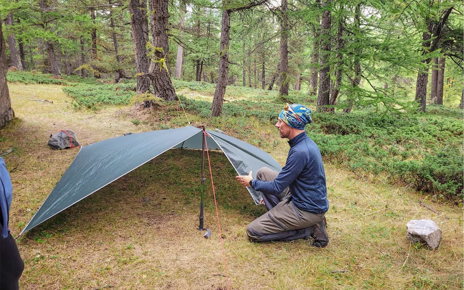 A participant prepares to pitch a tent in the lush Ubaye forest.