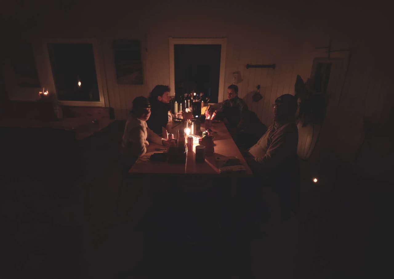 A group of travellers around a candlelit table, a warm atmosphere in Lapland.