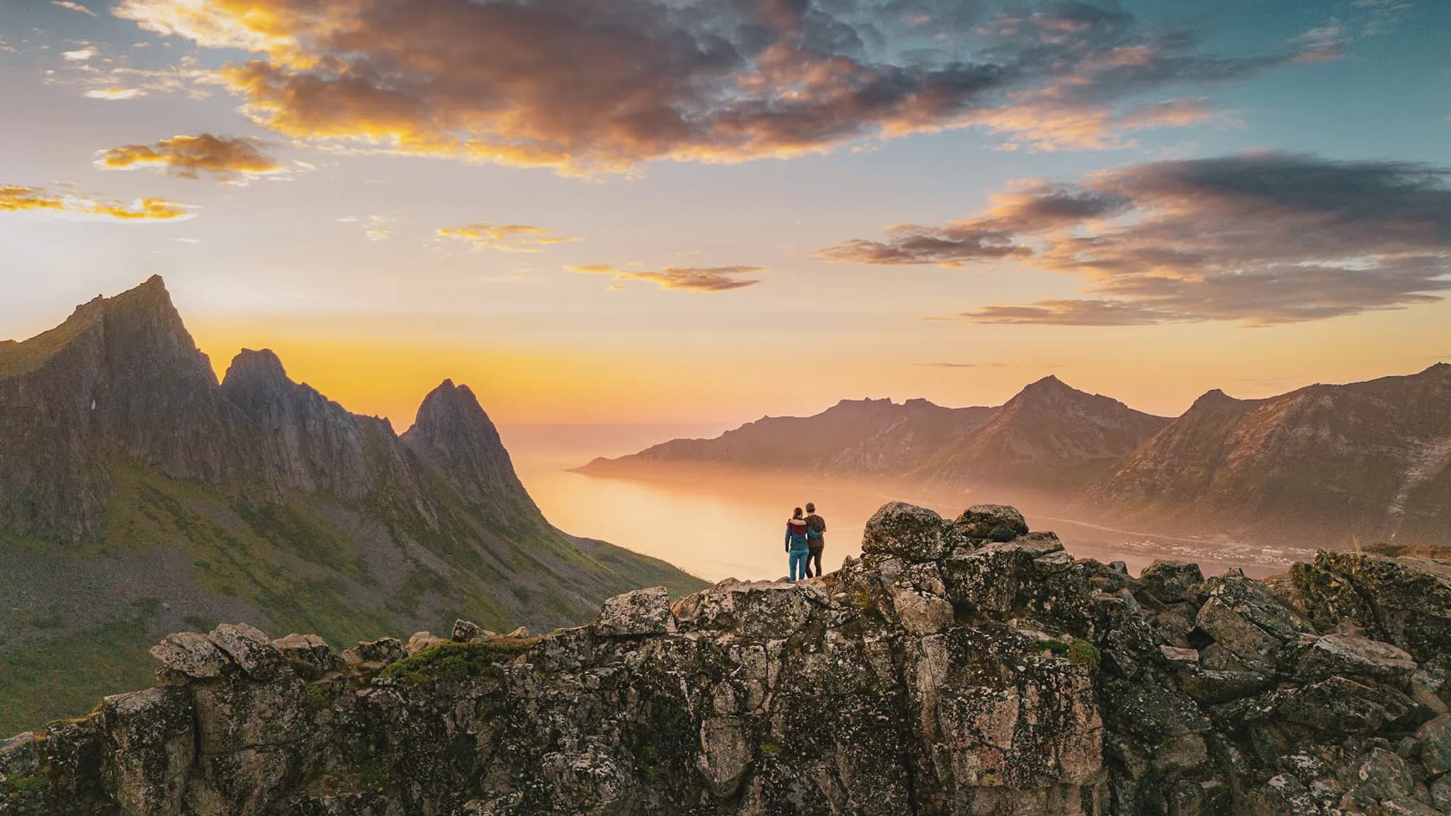 Couple admiring the sunset over the majestic peaks of Senja island.