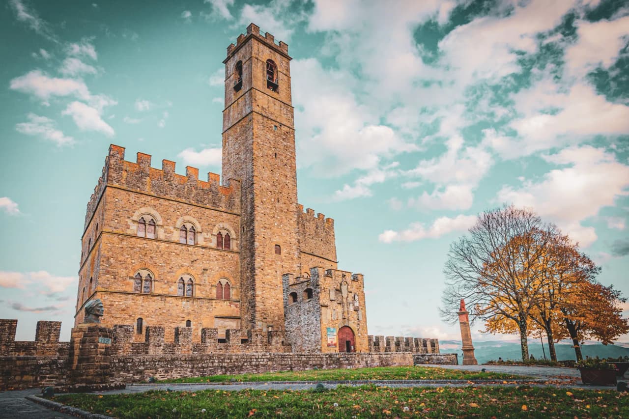 Poppi Castle in Iatlia, a stone castle with an imposing tower, set in greenery with a golden-leaf tree.