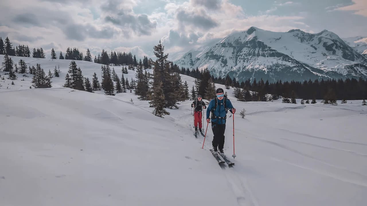 Skiers progress through a snow-covered landscape with majestic mountains in the background.