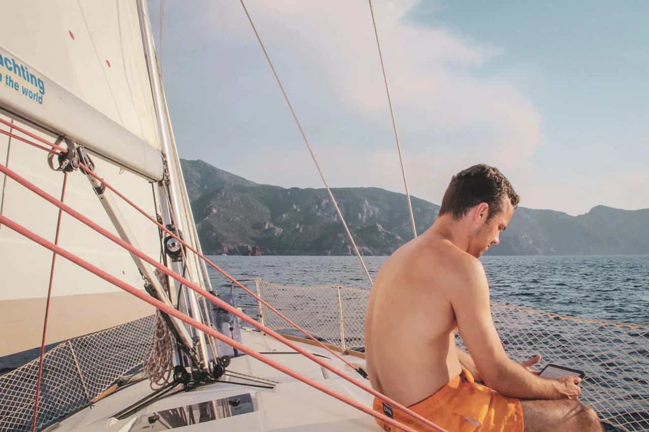 Navigateur en maillot sur un voilier, admirant les paysages côtiers de la Corse.
