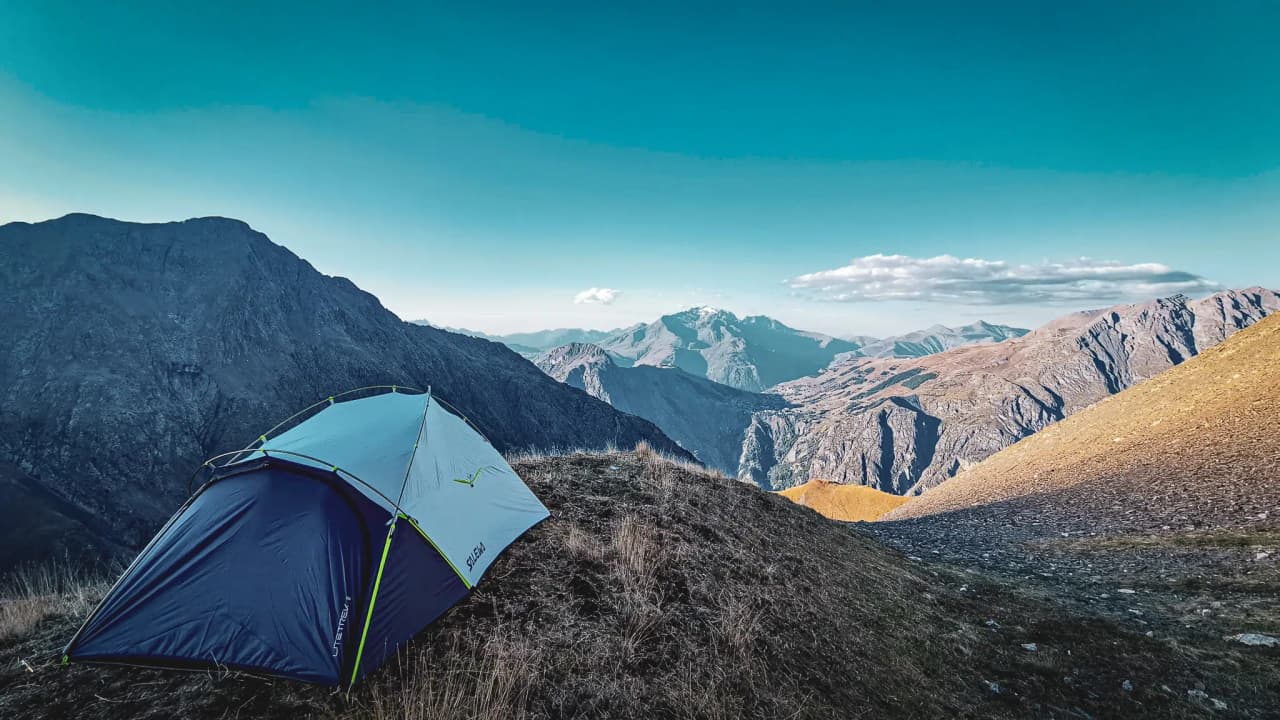 Tente colorée sur un sommet escarpé avec un panorama spectaculaire des montagnes environnantes.