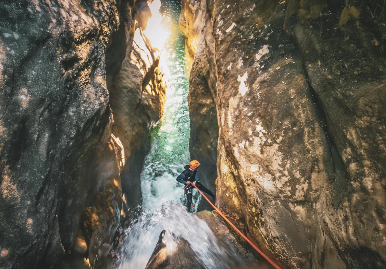 An adventurer in a diving suit descends a narrow gorge, guided by majestic rocks and sparkling water.