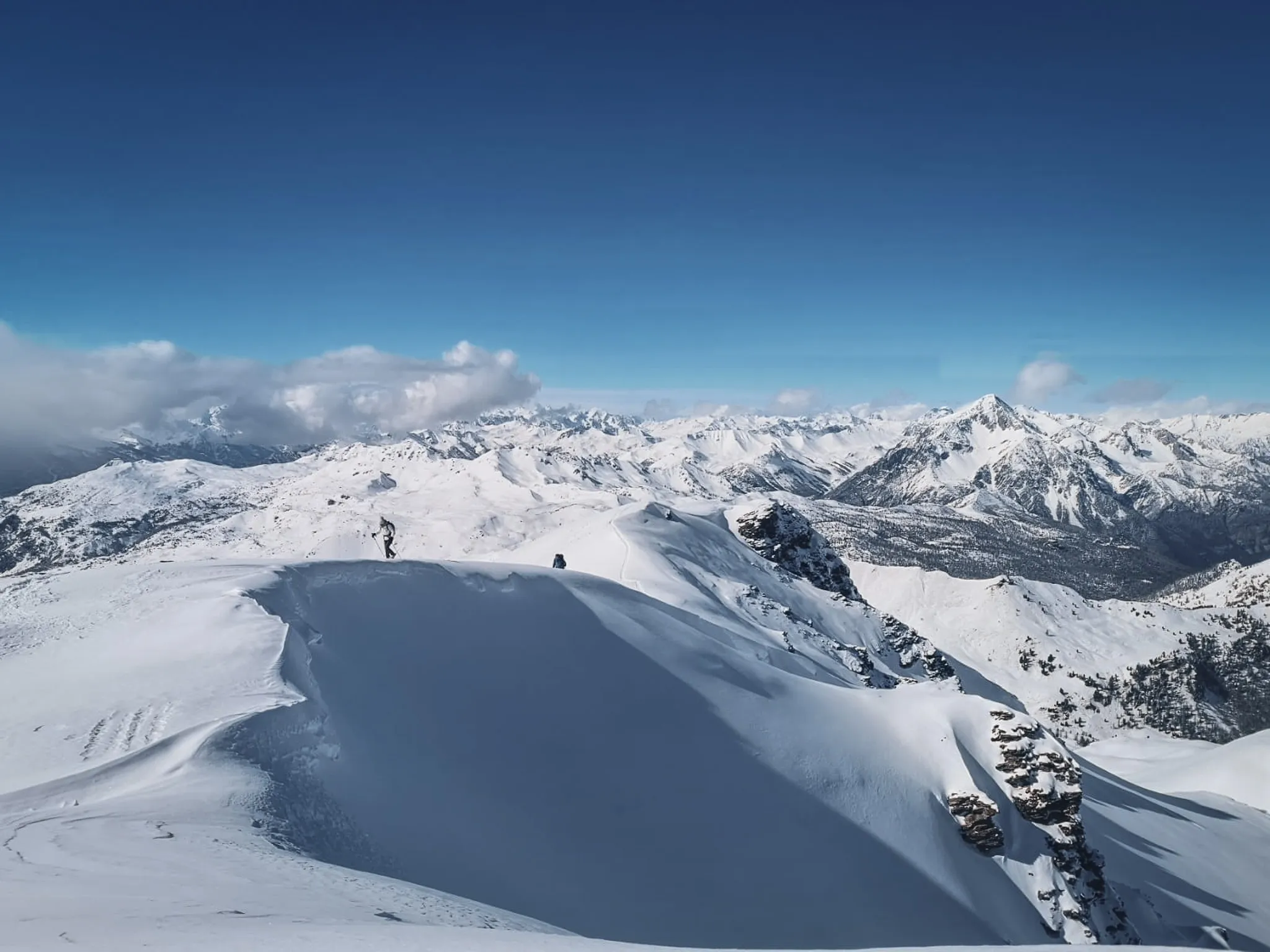Vast snow-covered landscapes, skiers on a ridge, brilliant blue skies between France and Italy.