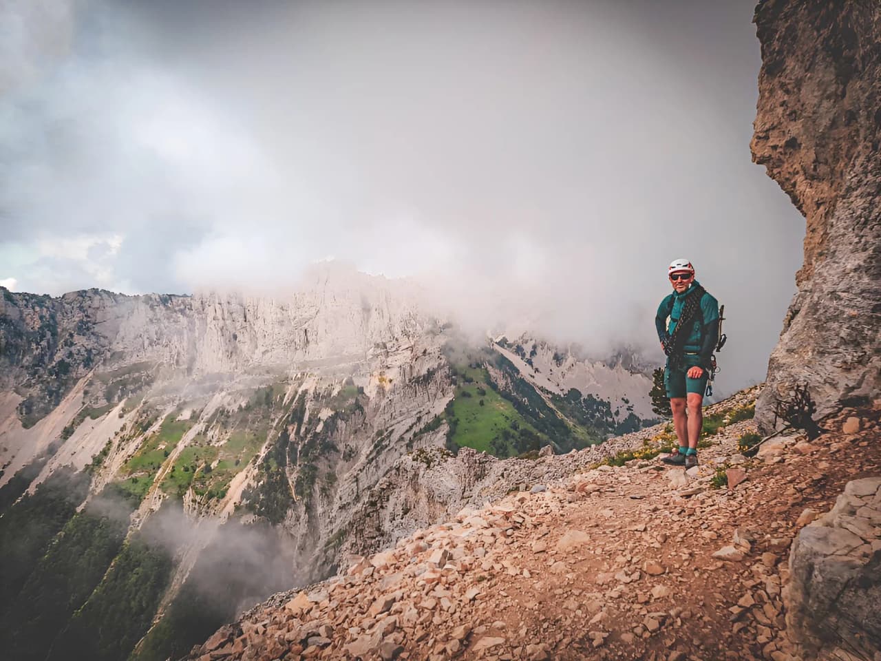 A smiling mountaineer on a steep trail, with Mont Aiguille and breathtaking scenery.