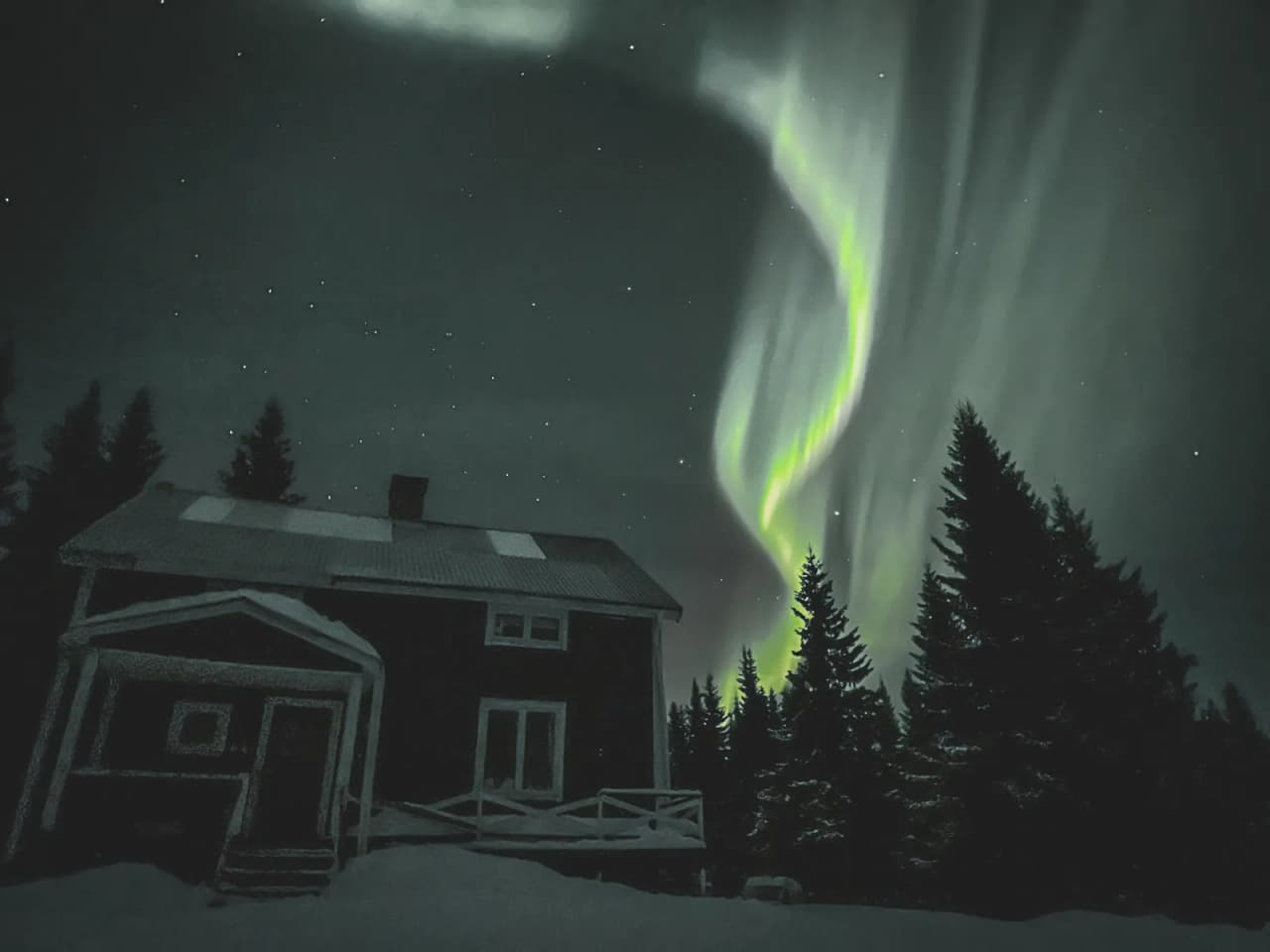 Aurores boréales illuminant le ciel au-dessus d'une maison enneigée en Laponie.