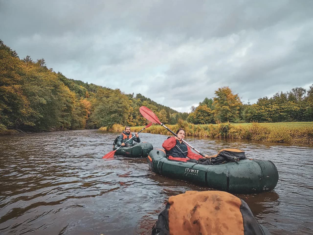 Een avonturier peddelt met een packraft op een rustige rivier, omgeven door weelderig groen.