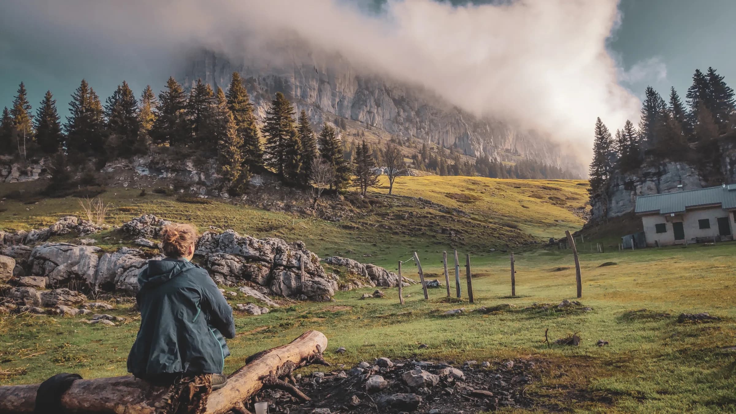 Randonneur contemplant un paysage verdoyant, entre rochers et majestueuses montagnes enveloppées de brume.