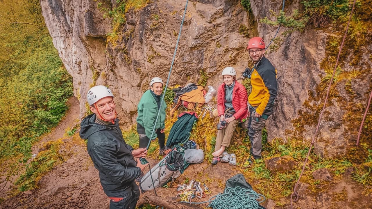 Groupe d'escaladeurs souriants préparant leur aventure en falaise, entourés de verdure.