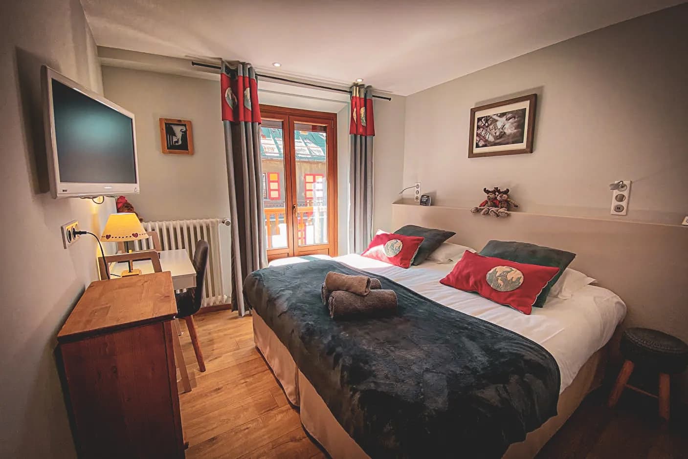 Une chambre cosy et accueillante avec un lit double habillé de couettes douillettes et de coussins ornés de motifs animalins. Un mobilier en bois, comprenant une table de nuit et un bureau, s'harmonise avec le sol