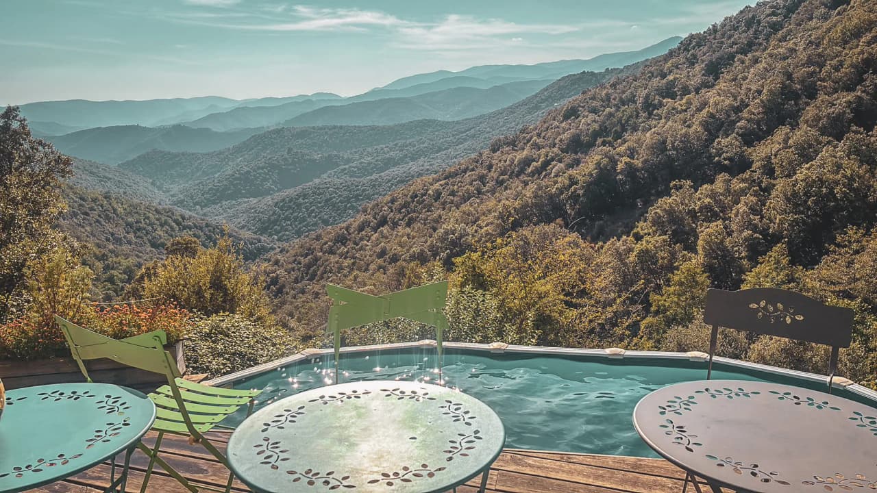 Vue panoramique sur les Cévennes, avec une piscine et des chaises colorées, invitant à la détente.