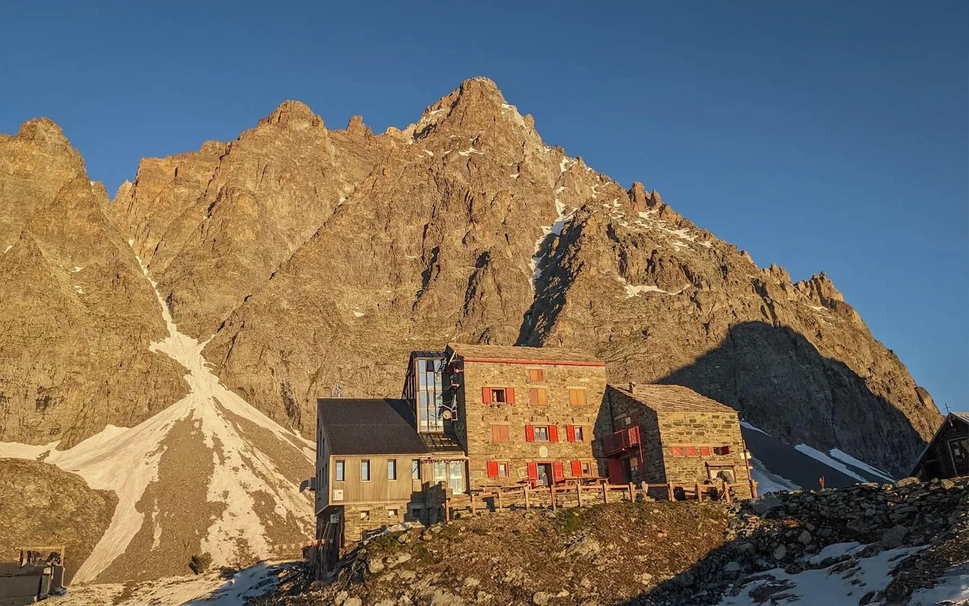 Mountain hut under a blue sky, with majestic Mont Viso in the background.